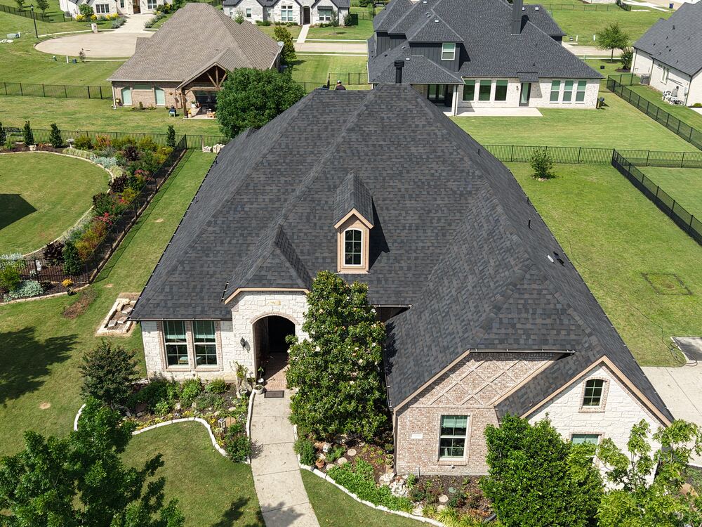 Completed dark shingle roof on stone home, aerial drone view