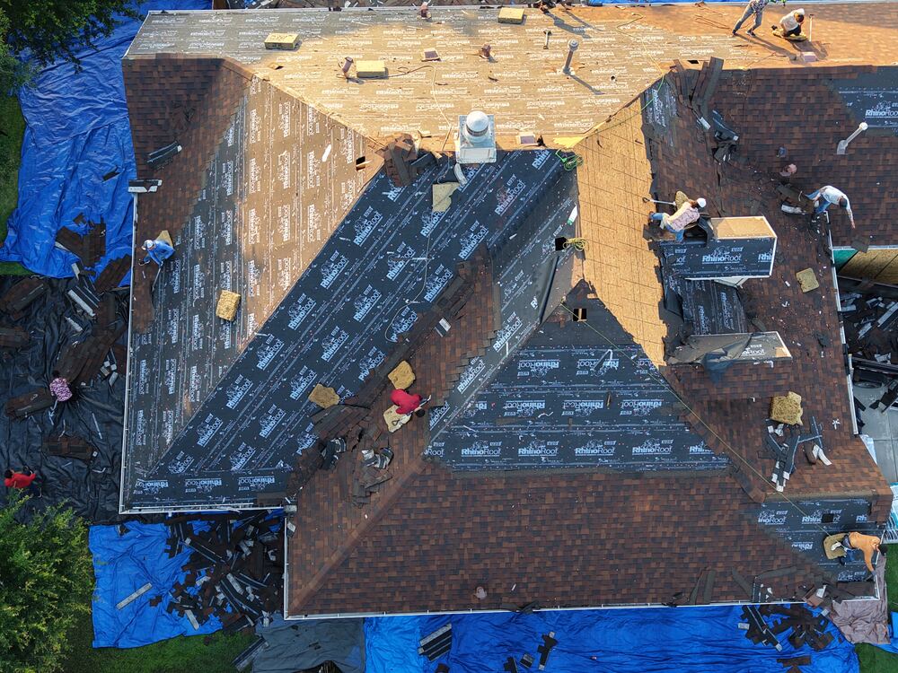 Full roof tear-off with crew installing underlayment, aerial drone view