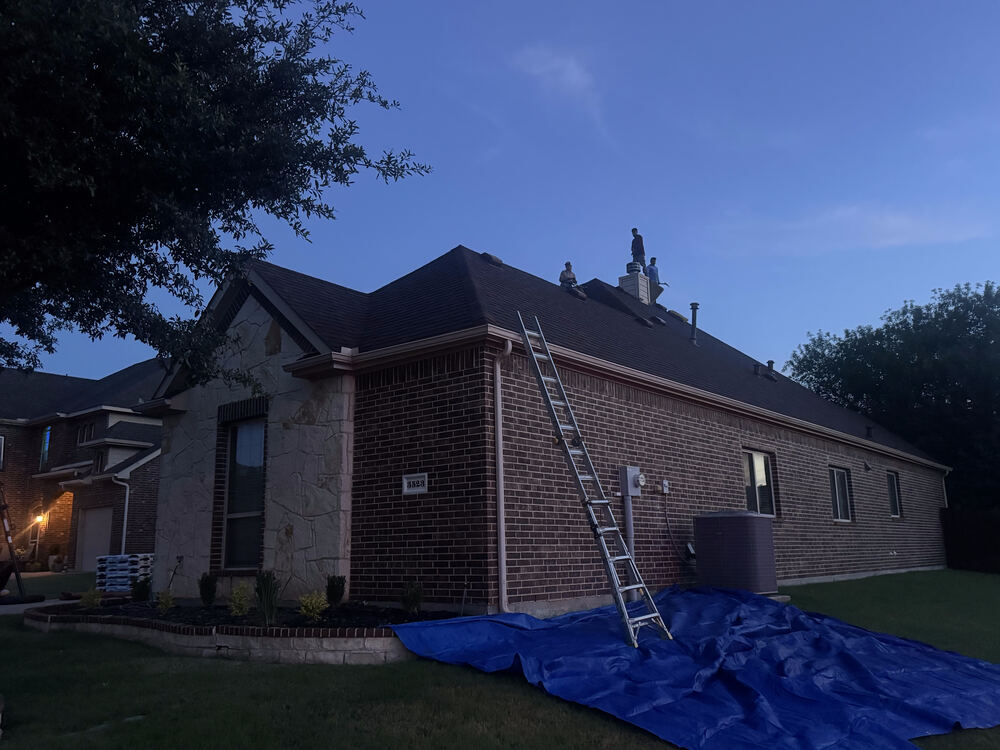 Crew working on roof at dusk with ladder and tarp